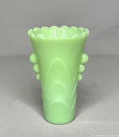 Front view of the Fire King jadeite green vase showing scalloped rim, glossy opaque pale green glass, and decorative raised bead accents on the side