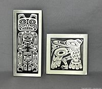 Photo of two vintage aluminum wall plaques with black First Nations art by Orchard Studio, one tall vertical figure and one square bird design.