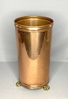 Front and side views of a cylindrical vintage copper umbrella stand with three claw feet. Some wear, light scratches and patina are visible on the surface.