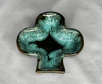 Top down view of clover-shaped glazed pottery ashtray in green and black glaze, showing pattern and shiny surface.