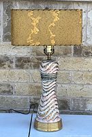 Front view of the vintage ceramic table lamp showing textured waves in white, pink, and gold on the base, brass pedestal base, and rectangular yellowed fiberglass shade.
