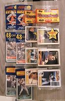 Four 1989 sealed baseball rack packs arranged on a flat surface. Two Score rack packs visible with blue and yellow branding, each containing 48 cards. Two Topps rack packs with orange and yellow branding, each with 42 cards. Packs are unopened, showing packaging design and card quantity details.