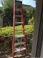Full image of orange fiberglass folding step ladder with aluminum steps in outdoor setting.