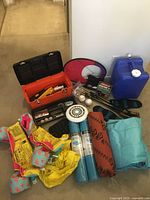 Wide view of the assorted camping and sports equipment including toolbox, weights, mats, air mattress, water jug, and frisbee