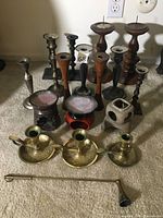 Full view of collection on floor including tall, short, brass and wood candlesticks and two burner-style holders.