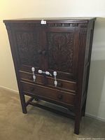 Full view of the carved wood cabinet showing front doors and drawers.