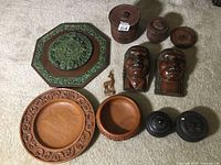 Overall view of nine wooden carved decor items including plates, jars, carved faces, a deer figure, and an octagonal green-accented wall plaque.