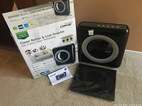 Air purifier, original box, spare filter and user manual on carpeted floor.