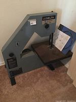 Full view of the Delta band saw showing the machine body, front panel, and work table with parts list on it.