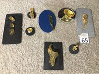 Overall view of collection of eight handcrafted amber artwork pieces on different colored bases, showing size and shape variety