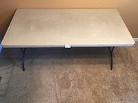 Top view of the white rectangular folding table on carpeted floor, showing surface condition and size.