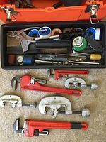 Top-down view of toolbox lid opened showing plumbing tools and pipe wrenches arranged beside the box