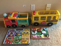 Two plastic toddler vehicles (school bus and recycling truck) with two wooden latch puzzles.