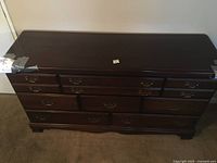 Top front view of the wide dark wood dresser with eight drawers and taped corners for child safety.