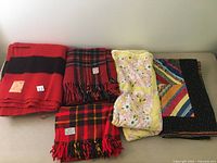 Full view of three wool blankets and two baby quilts laid out on table.