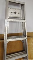 Front view of the folded aluminum ladder showing wide steps and top platform.