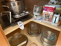 Wide view showing metal colander, muffin tin, several glass mixing bowls, measuring cup, and cookie cutter box.