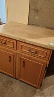 Overall view of the wooden kitchen cabinet with butcher block top, showing the two drawers and two doors with metal handles in a medium oak finish.