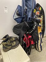 View of two folding camp chairs, a pair of boots on top of a cooler, black and yellow board with stickers, and a black camping lantern.