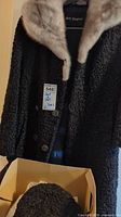 Black textured faux fur jacket with light beige fur collar hanging on a hanger, Holt Renfrew label visible, size S tag attached
