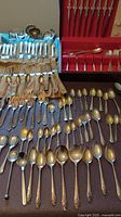 Overview of assorted flatware including forks, spoons, knives, some organized in box and others laid out on surface