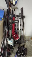 Multiple golf clubs in red/black stand bag with push caddies in garage floor