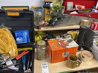 Photo of various tools on a table including a large hand saw, Black & Decker palm sander box, a tool box, a jar with screws, and other hardware.