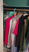 Photo of assorted jackets and tops on hangers, colors include bright pink, white, beige, black with pinstripes, and olive green.