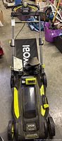 Front view of assembled Ryobi mower with handlebar folded, grass bag attached, battery and charger placed on deck.