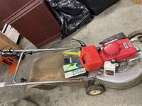 Overall view showing mower, grass bag, fuel can and oil bottle