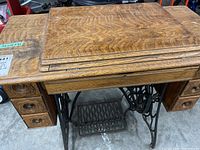 Closed oak cabinet with visible wood grain and three drawers on each side; cast iron treadle base at the bottom.