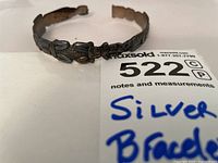 Sterling silver Indigenous design bracelet shown on white background with identification tag.