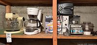 Shelf with all small kitchen appliances including the Sunbeam Mixmaster, Black & Decker coffee maker, Osterizer blender, Oster toaster, Proctor Silex steam iron, and manual ice cream maker.