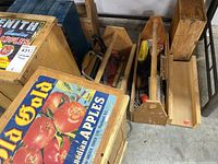Two wooden apple boxes with vintage commercial apple crate labels on top. One has a broken slat, along with two wooden carpenter totes filled with various tools and a small hardware storage box.