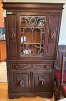 Front view showing carved details, glass door with etched pattern, drawer, and lower cabinet with carved doors.