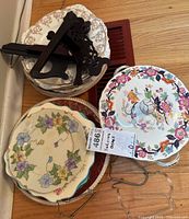 Stack of assorted vintage plates including floral patterned and two-tiered plates with a wooden display stand on top.