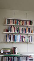 Three shelves of assorted books of various sizes and colors arranged upright and stacked horizontally on shelves