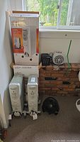 Lot overview showing three Classic oil filled heaters, two still boxed, and three compact space fans on a brick hearth.