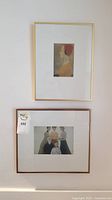 Photo of two framed art prints on wall; top depicts a profile portrait of a woman with red hair, bottom is a group portrait of five women in muted tones.