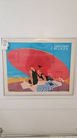 Front view of the entire framed art print showing the image of two women under a large red umbrella on a beach with the text 'East Coast by L.N.E.R'.