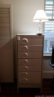 Full view of off-white Treco dresser with circular recessed drawer pulls and lamp on top