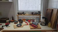 Overview of kitchen items on counter and shelf including wooden cutting boards, small bowls, chopsticks, electric kettle, and cooking oil.