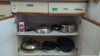 Shelf with multiple pans and pots including a stainless steel pot with lid, small saucepans, cast iron skillet, and seasoning container