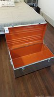 Open metal trunk showing orange enameled interior and metal exterior with latches