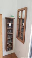 Side view of narrow distressed wooden shelf holding assorted clear glass drinking glasses with tall mirror mounted next to it.