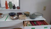 Pottery items displayed on shelves including bowls, dishes, and vases with kitchen linens visible in a drawer below.