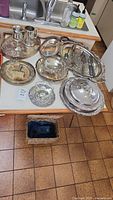 Full view of the silver plate collection displayed on a counter, showing trays, goblet, pitcher, covered dish, bowl, brush and plates.