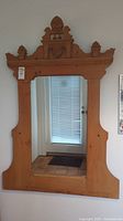 Full view of the wooden framed mirror hanging on a wall in front of a door with a window.