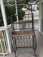 Full view of the wrought iron bakers rack showing three wood shelves and the decorative metal scrollwork frame.