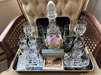 Full set of crystal barware including decanter with stopper, multiple glasses, and coasters arranged on a chair.
